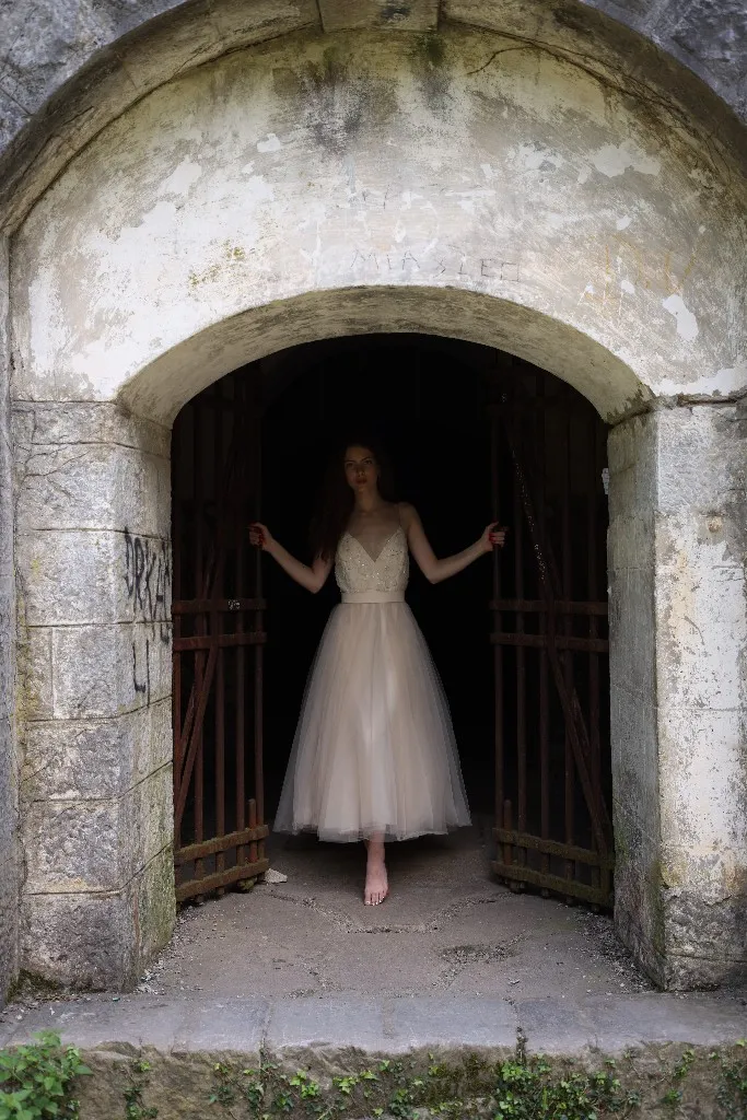 Model in a pale tulle gown standing in a weathered stone archway