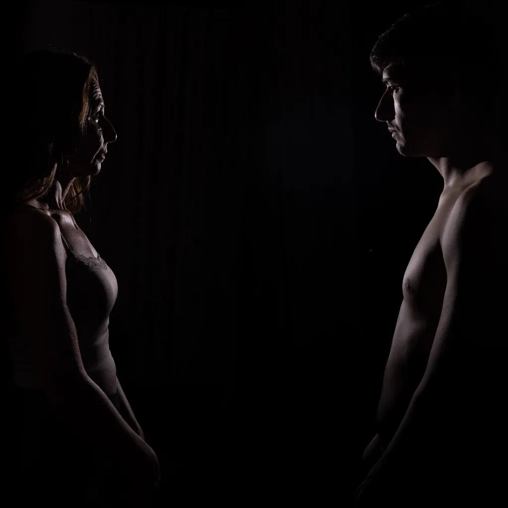 A woman and a man facing each other in profile, lit low against black