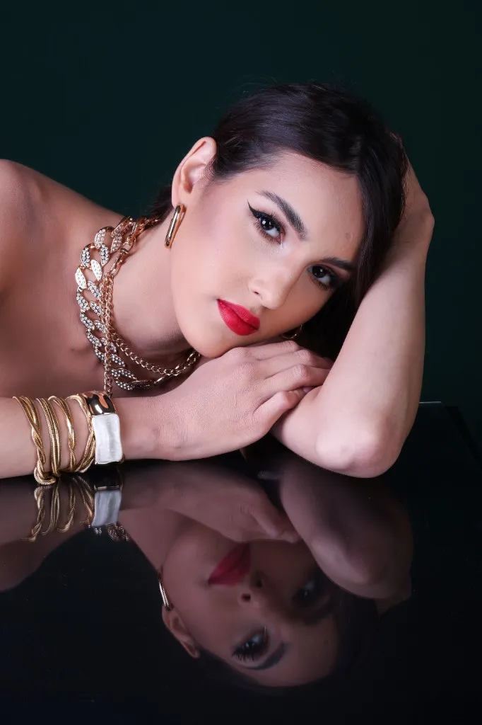 Studio beauty portrait in gold jewelry, mirrored on black glass