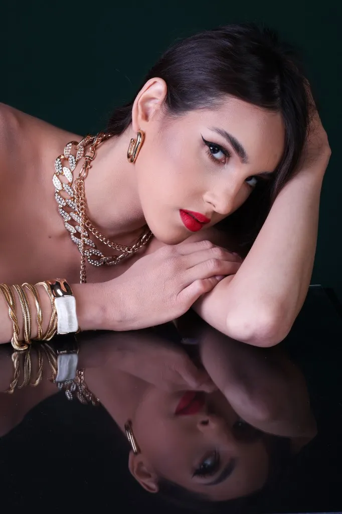 Model with hands beneath her chin, steady gaze, gold chains