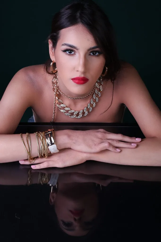 Model with arms resting on the glass, chunky gold chain, direct gaze