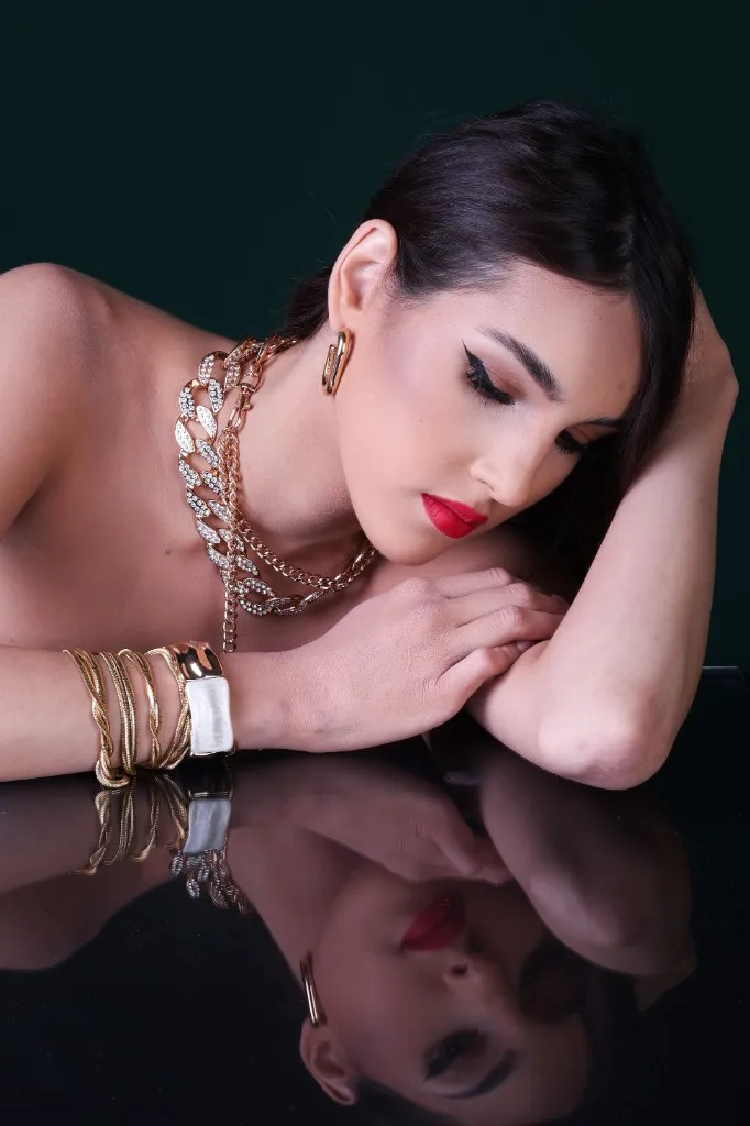 Model with eyes lowered, gold jewelry, reflected on black glass