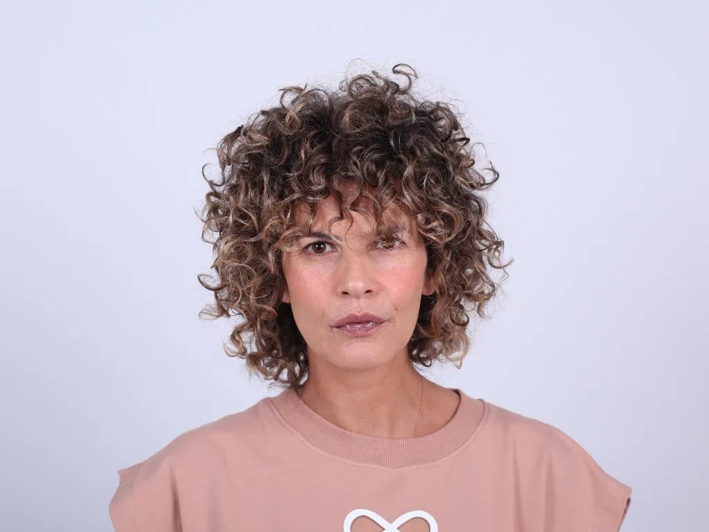 Woman standing to camera in a dusty-pink top, hands at her sides, composed
