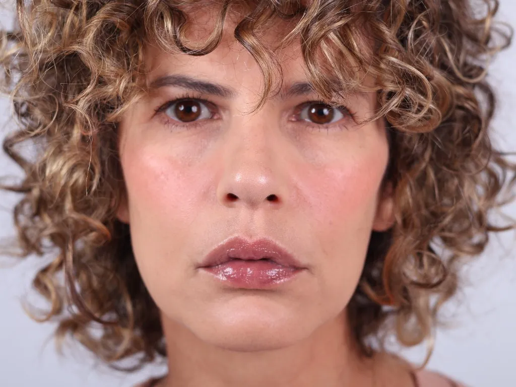 Studio portrait of a woman with curly hair, a steady, sober gaze to camera