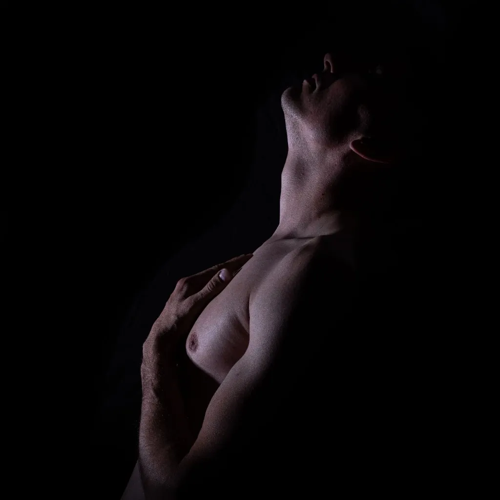 A figure emerging from darkness, throat and chest catching a low light