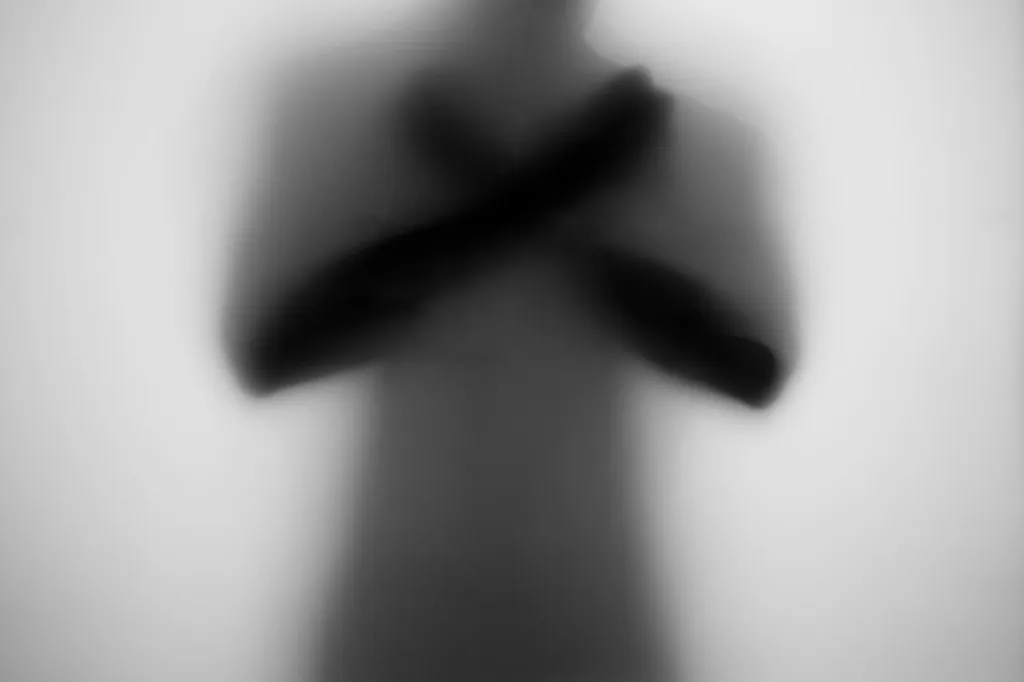 A figure with arms crossed over the chest behind frosted glass