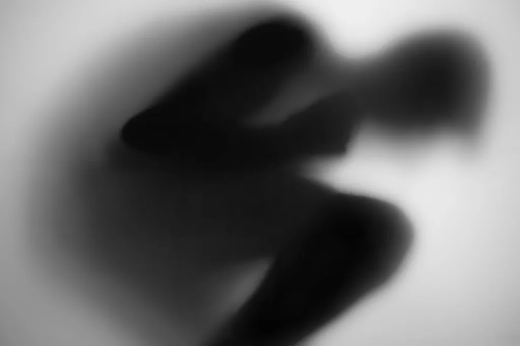 A crouched figure curled into a dark abstract form